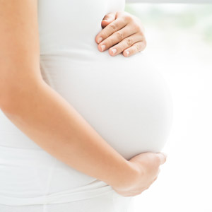 Woman wearing a white shirt holding her baby bump.
